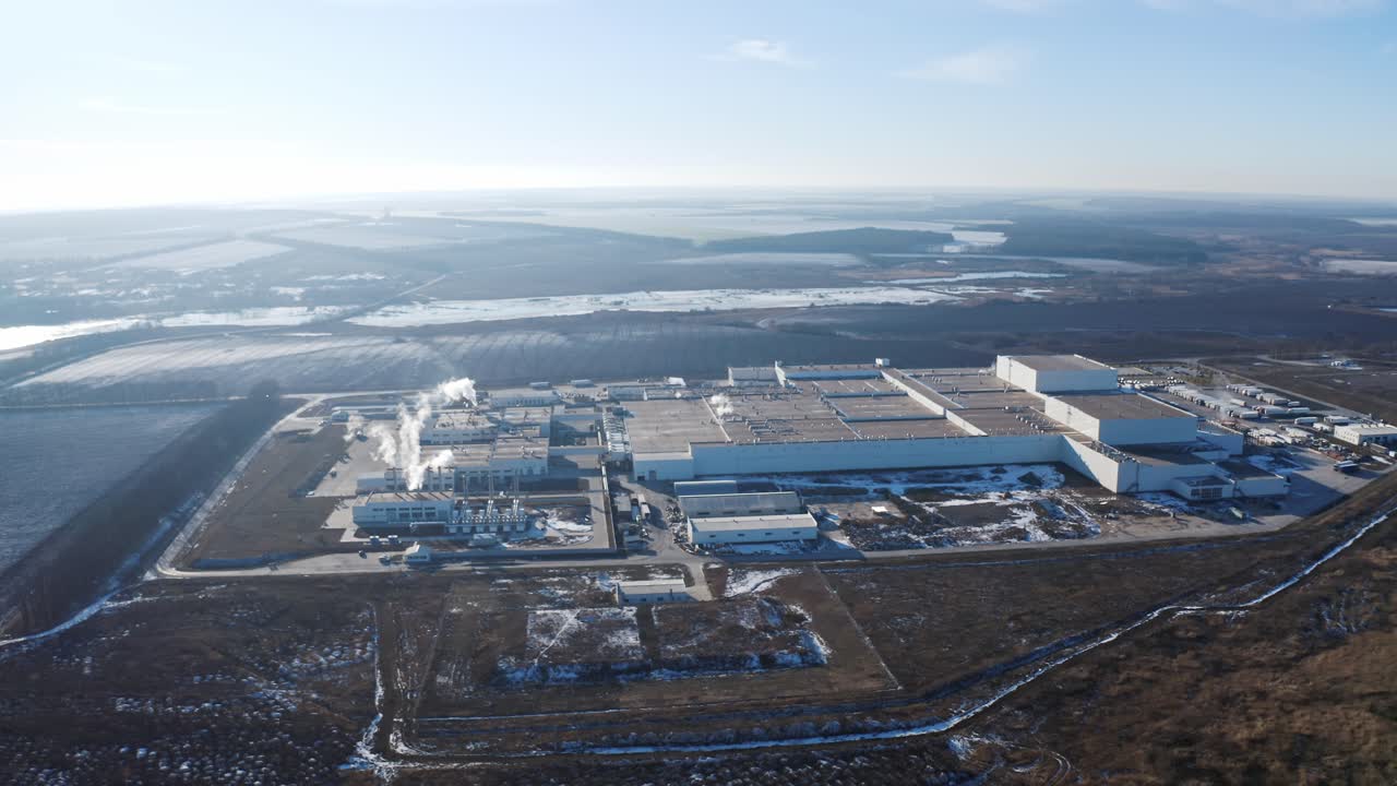 Huge industrial plant among nature. View from the air on a modern factory surrounded by fields and forests in winter time. Aerial view.