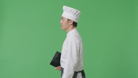 side view of asian man chef holding a tablet while walking in the green screen background studio