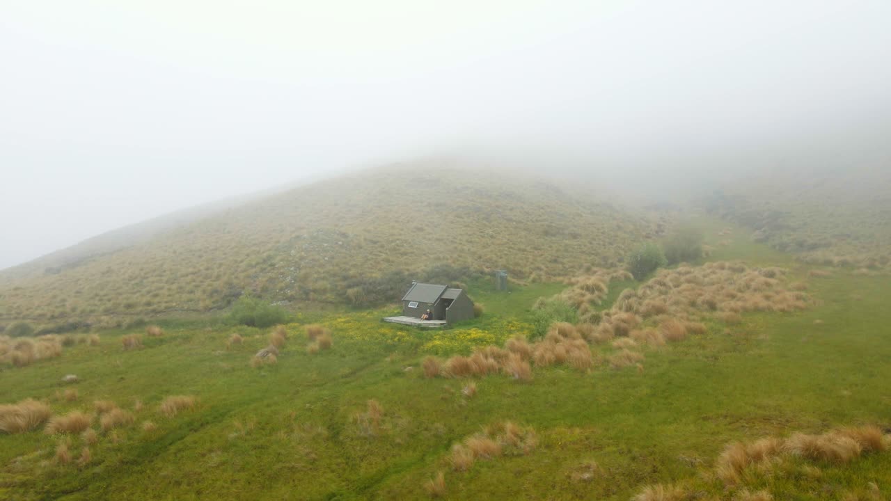 낮은 안개를 배경으로 언덕이 있는 푸른 평원에 있는 등산객의 오두막