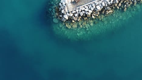 Gente-Buceando-En-El-Mar-Azul-Cristalino-Desde-Un-Puerto-Deportivo-Con-Rocas-A-Su-Alrededor