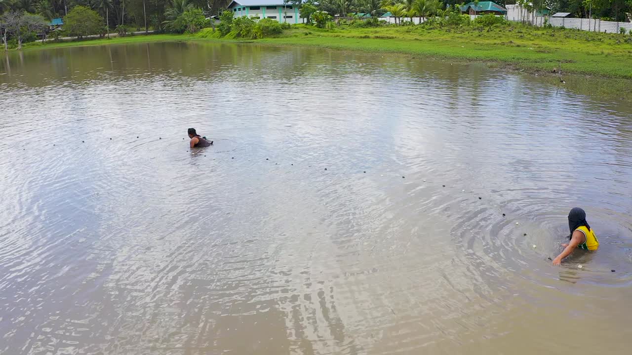 Aerial view across group of men adjusting nets in tropical lagoon water. Dark patterns created underwater from disturbed ground. Bohol, Philippines.