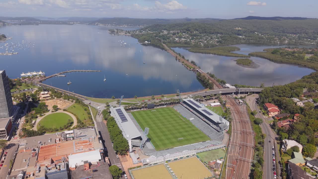 Wide aerial ascend orbit of Polytech Stadium in Gosford with visible stands, field, and nearby coastline, Central Coast NSW Australia