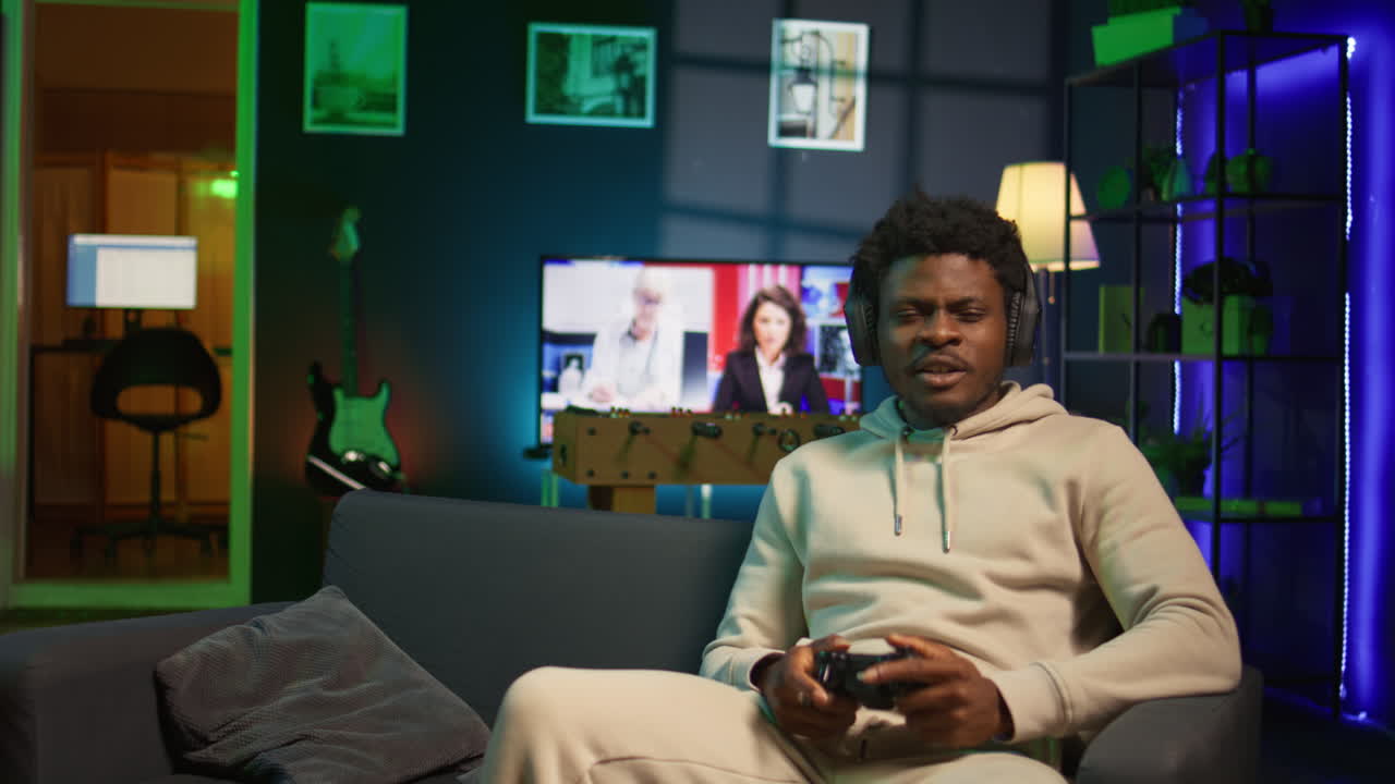 African american adult using headphones mic to talk with teammates while playing video games in cozy apartment. Gamer chatting with internet friends while enjoying game on gaming console. Camera B.