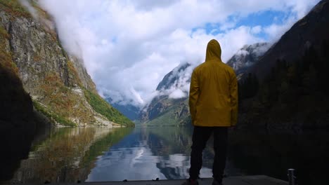 mann in einer gelben jacke steht auf einem kai, um den beeindruckenden sognefjord norwegens zu genießen