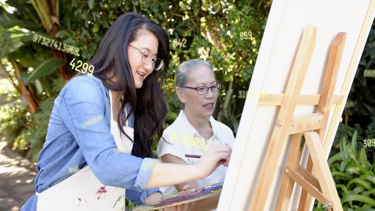 Mid adult woman applying paint at easel, senior woman watching and guiding for art mentoring