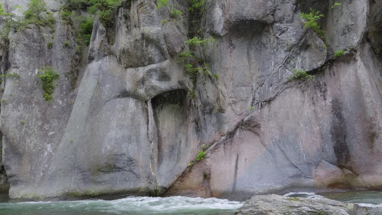 Slow motion tilt up over tall stone cliffs next to running river