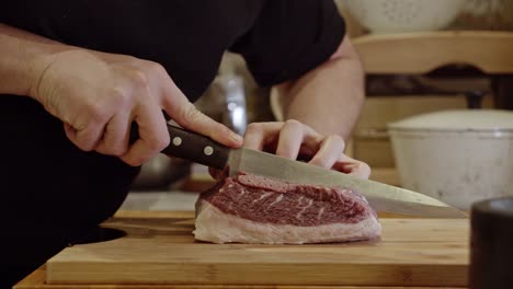 Slicing-the-steak-with-steel-kitchen-knife-against-the-nerve-on-wooden-cut-board