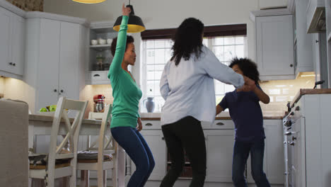 una pareja de lesbianas de raza mixta y su hija bailando en la cocina.