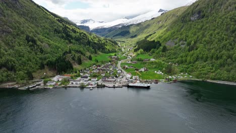 Beautiful-town-of-Eidsdal-More-and-Romsdal-with-mountain-valley-behind-and-ferry-alongside-pier---Springtime-aerial-with-lush-green-hillsides-and-snow-capped-mountains---Norway