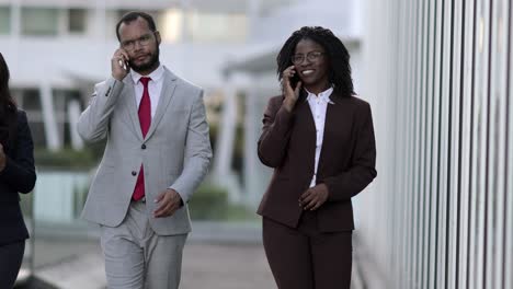 smiling managers walking on street and talking on smartphones