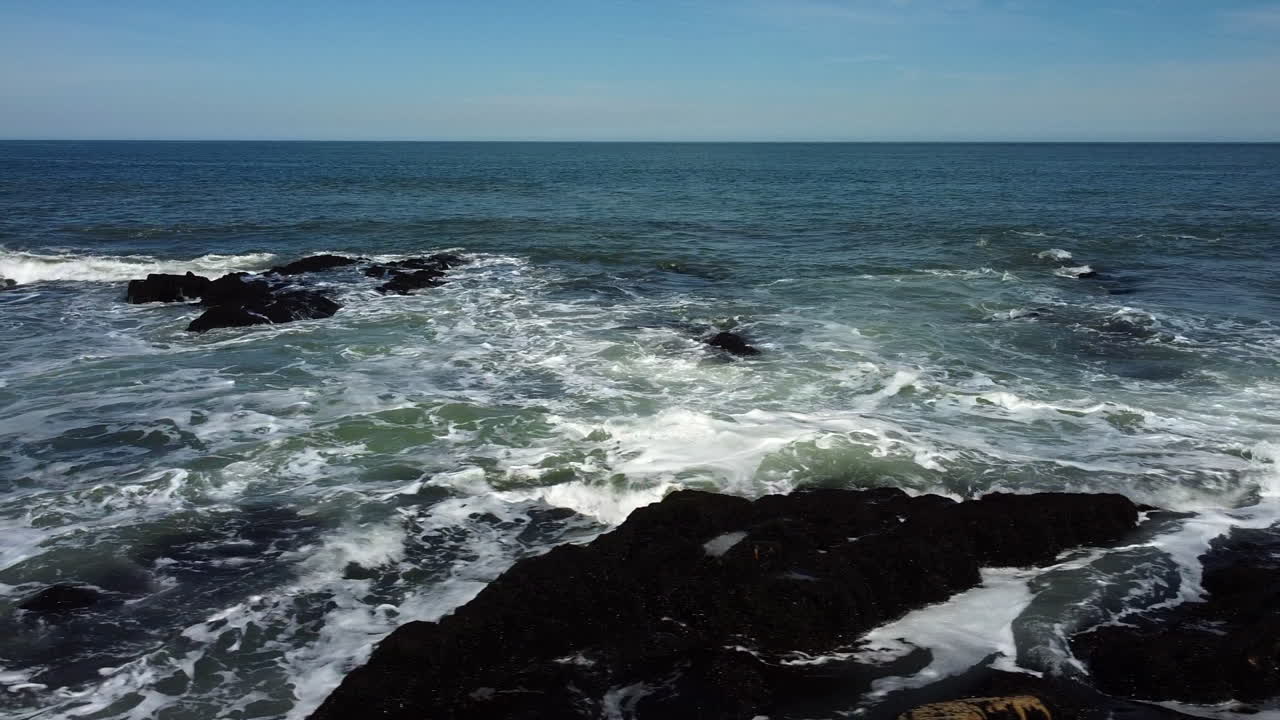 Drone footage flying sideways over rocks and waves breaking with sea bird taking off and flying away