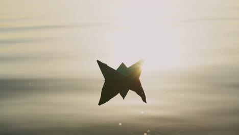 paper boat floats alone with its reflection on the wavy water in the river at sunset. beautiful rays of the evening sun falling on origami ship.close-up