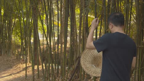 un hombre que camina por un jardín de bambú se quita el sombrero para picar el cuero cabelludo y quitarse la caspa de la camisa