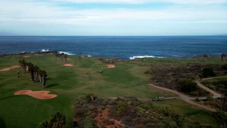 Luftschwenkaufnahme-Eines-Grünen-Golfplatzes-An-Der-Küste-Spaniens,-Tagsüber-Blaues-Meerwasser