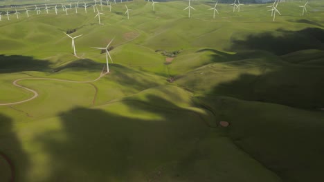 aerial shot of clouds rolling on green hills revealing wind turbine at altamont pass on vasco road highway with green rolling hills in california