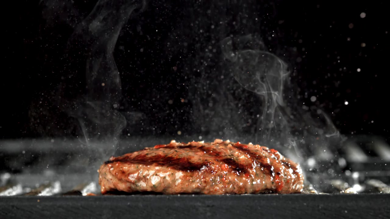 Slowmotion nærbillede af en burgerbøf, der syder på en varm grill