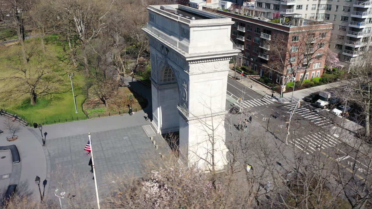 Una veduta aerea dell'Arco di Washington Square a New York. La telecamera del drone orbita a destra, in senso antiorario attorno all'arco. Il parco e le strade circostanti sono vuoti; è una giornata luminosa e soleggiata.