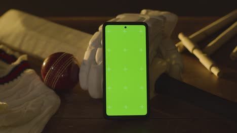 green screen mobile phone surrounded by cricket bat ball and clothing on wooden surface 3