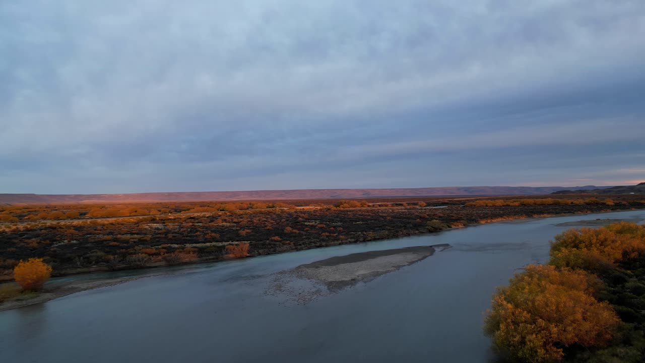 Drone panorama of a glowing sunset over Patagonia, with a deep blue river winding through the vast Argentine Pampa