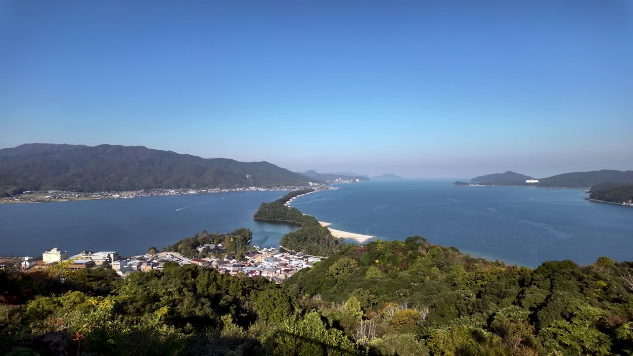Breathtaking view of Amanohashidate, a natural sandbar covered in pine trees, creating a scenic divide in the tranquil waters of Miyazu bay. slow tilt up shot