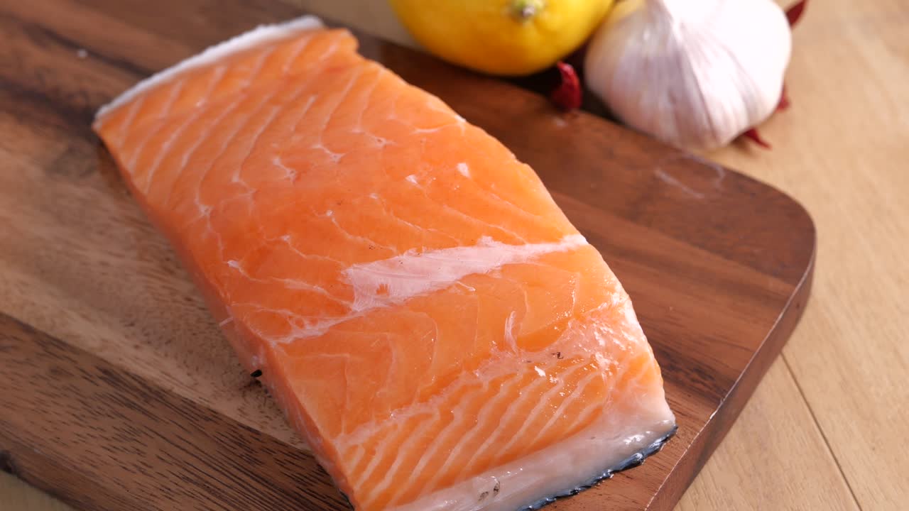 filete de salmón crudo en una tabla de cortar de madera con limón, ajo y chiles