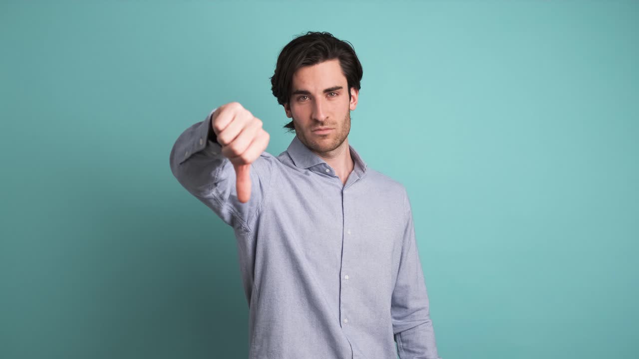 Upset man showing thumb down in blue studio