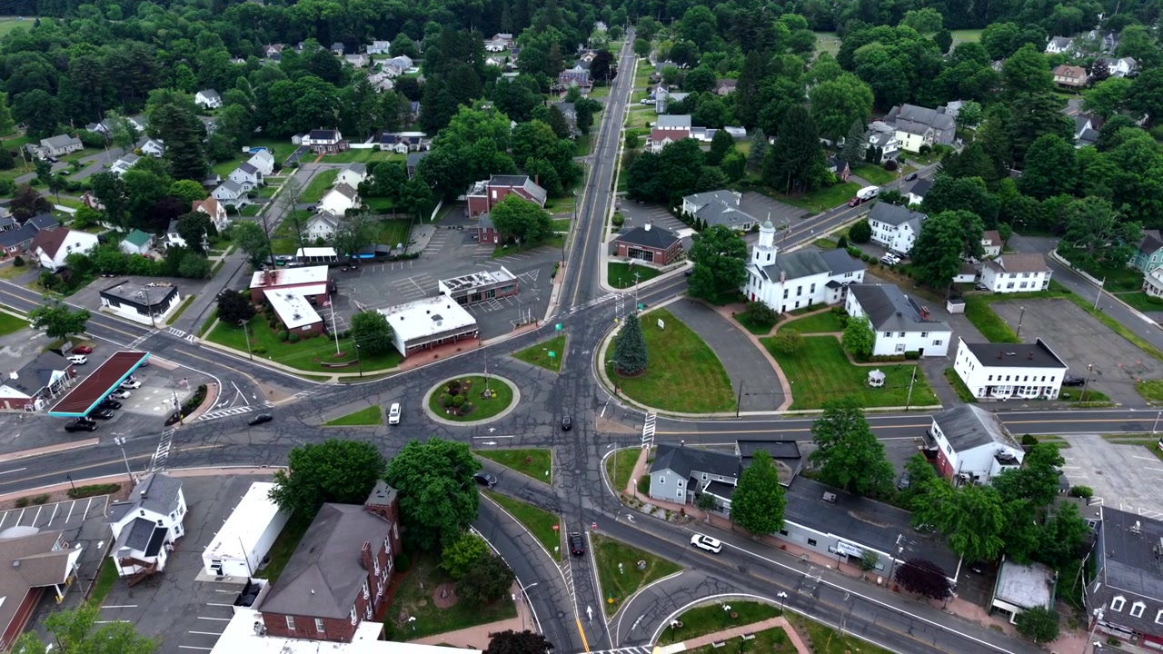 Ripresa aerea con drone in allontanamento sopra l'incrocio a rotatoria vicino al Municipio di East Longmeadow e a una chiesa bianca, che rivela una lussureggiante città suburbana verde con strade residenziali in Massachusetts.