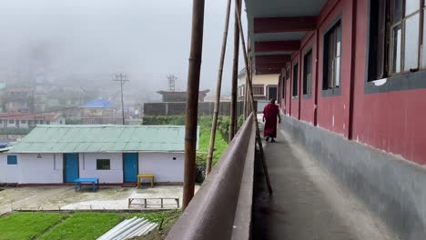 rear view of monk walking through temple columns inside a monastery with cloud covered hill town outside