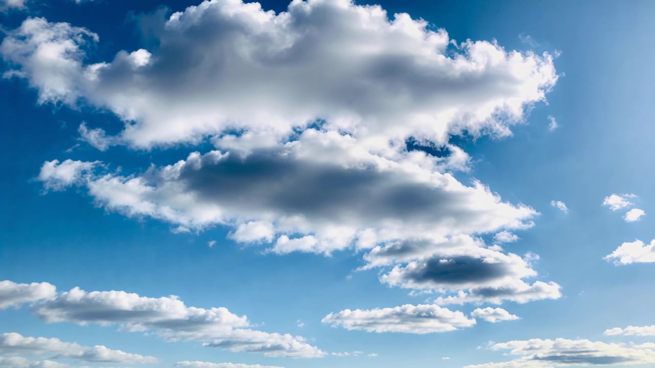 Gruppo di cumuli che si sposta e reagisce alla luce solare, assottigliandosi e perdendo filamenti nel cielo azzurro e limpido.