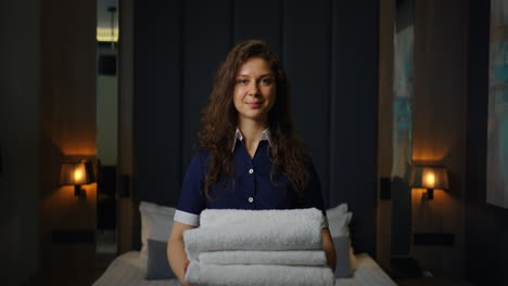 una doncella de hotel sonriente sosteniendo toallas limpias en una habitación de hotel