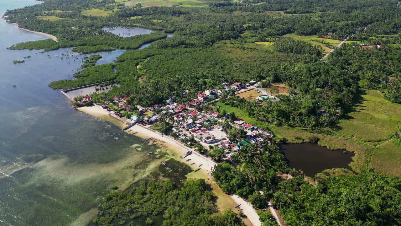 Picturesque flyover drone shot of peaceful shoreside barangay village surrounded by lush tropical island greenery - Yocti, Catanduanes, Philippines