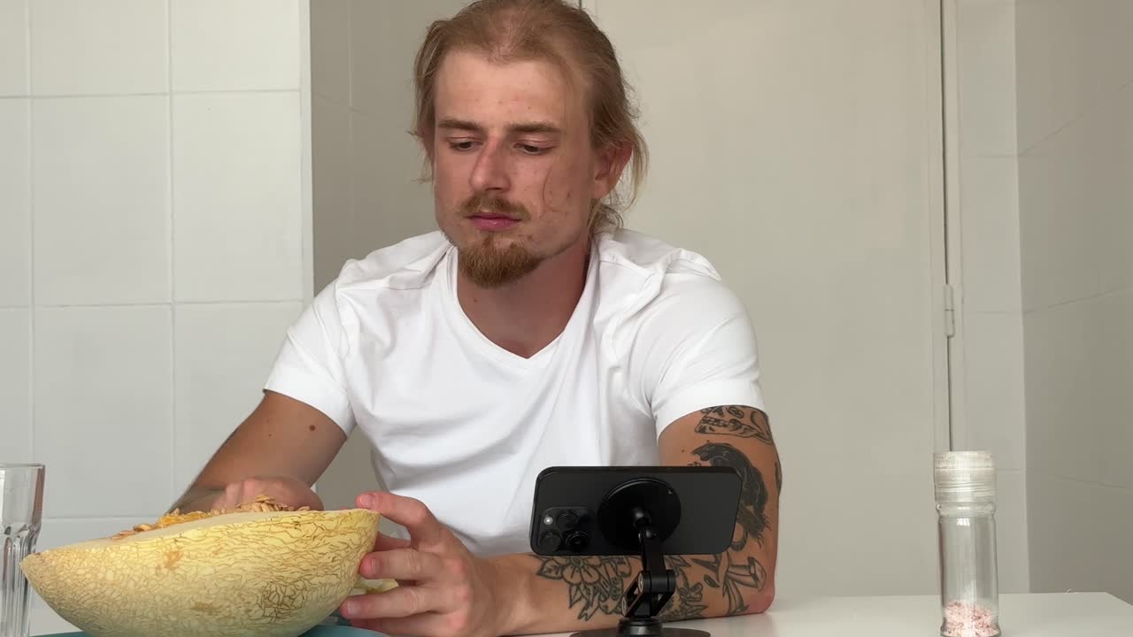 Ung mann spiser fersk melon mens han ser på smarttelefonen
