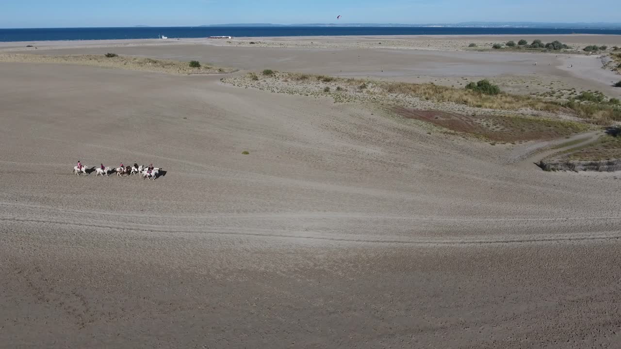 un grupo de jinetes en una playa disparado por un dron, una tarde soleada en francia.