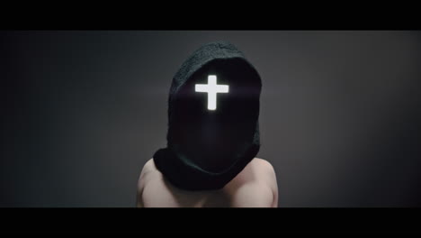 masked and hooded man with cross of light glowing on his face rise his arms
