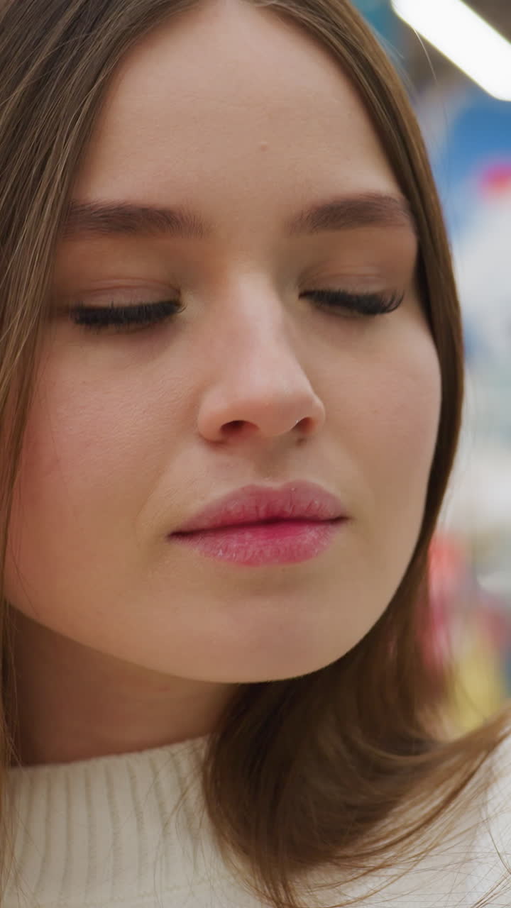 Close-up of woman with warm expression inspecting green shiny tinsel length in store with blurred background and bokeh light effect, carefully considering purchase for holiday decor