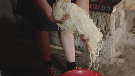 mujer campesina georgiana escurriendo cuerdas de cuajada de queso en un recipiente de plástico