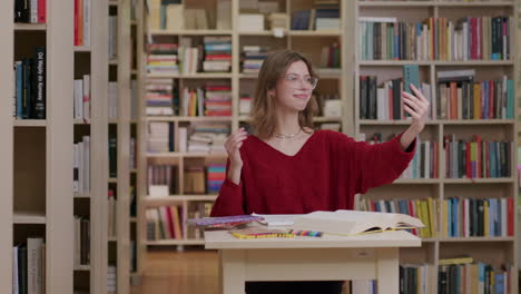 estudiar a una estudiante caucásica en la biblioteca toma una videollamada en un teléfono inteligente