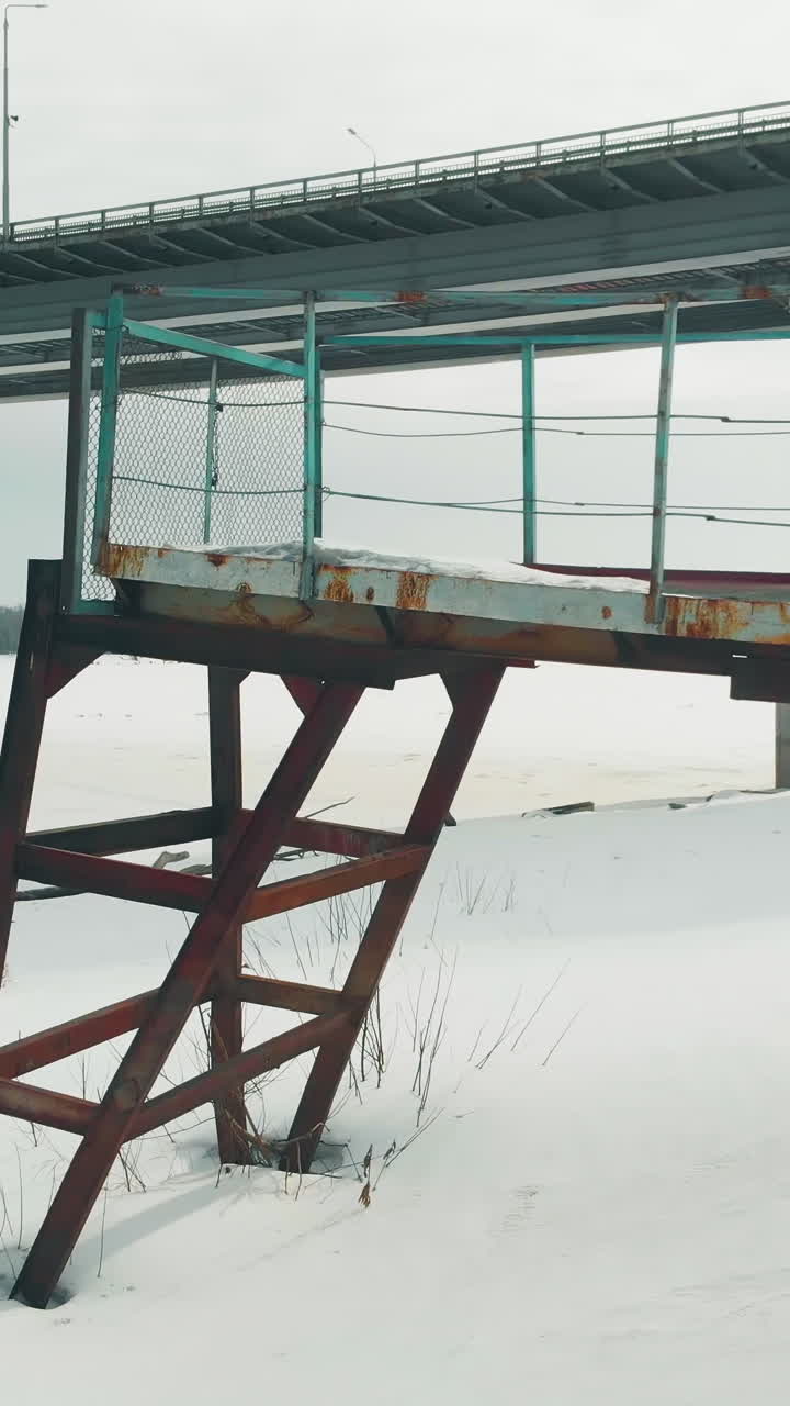 old rusty pier with unreliable support at white frozen river against large grey bridge aerial view