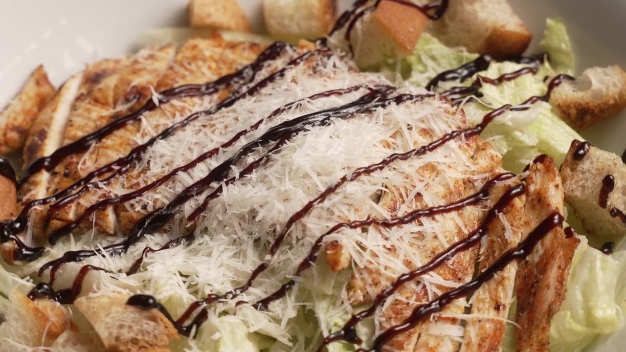 Deliziosa insalata Caesar di pollo che gira in una ciotola bianca con formaggio parmigiano e condimento balsamico