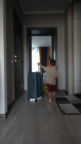 little boy goes by the house pushing a suitcase. vacation and travelling concept. vertical video.