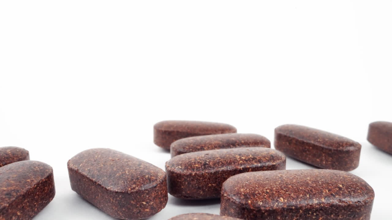 Close-up of brown herbal supplement tablets scattered on white background