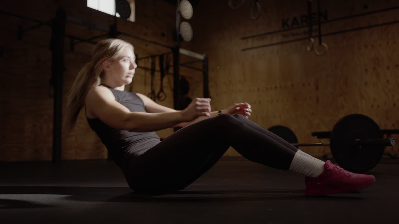 Ripresa in tempo reale di una bionda appassionata di fitness che fa addominali in palestra, con illuminazione cinematografica.