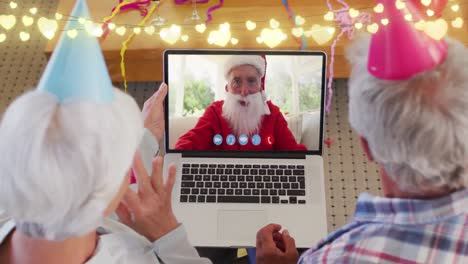 Animación-De-Luces-De-Colores-Sobre-Una-Feliz-Pareja-De-Ancianos-Caucásicos-En-Una-Videollamada-Portátil-Con-Santa-Claus