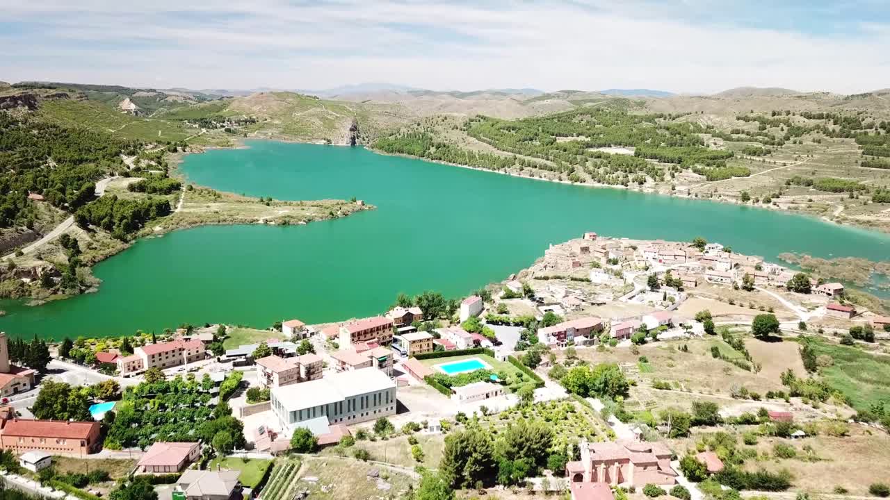 A scenic aerial view of Embalse de la Tranquera in Spain, featuring turquoise waters, surrounding greenery, and the charming village nearby, blending natural beauty with rural architecture