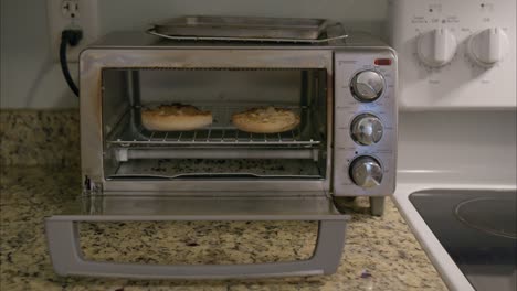 hands removing english muffin toast from toaster oven with a knife to make breakfast on a green plate