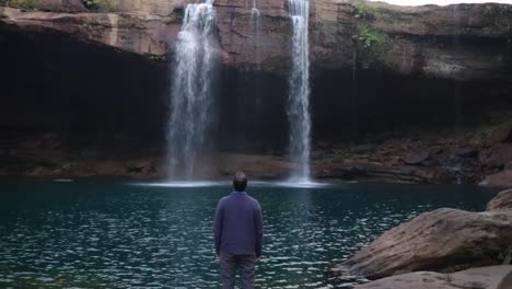 young man enjoying the natural waterfall falling from mountain top at morning video taken at krangsuri waterfall meghalaya india