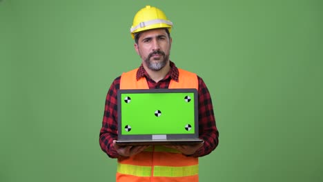handsome persian bearded man construction worker showing laptop