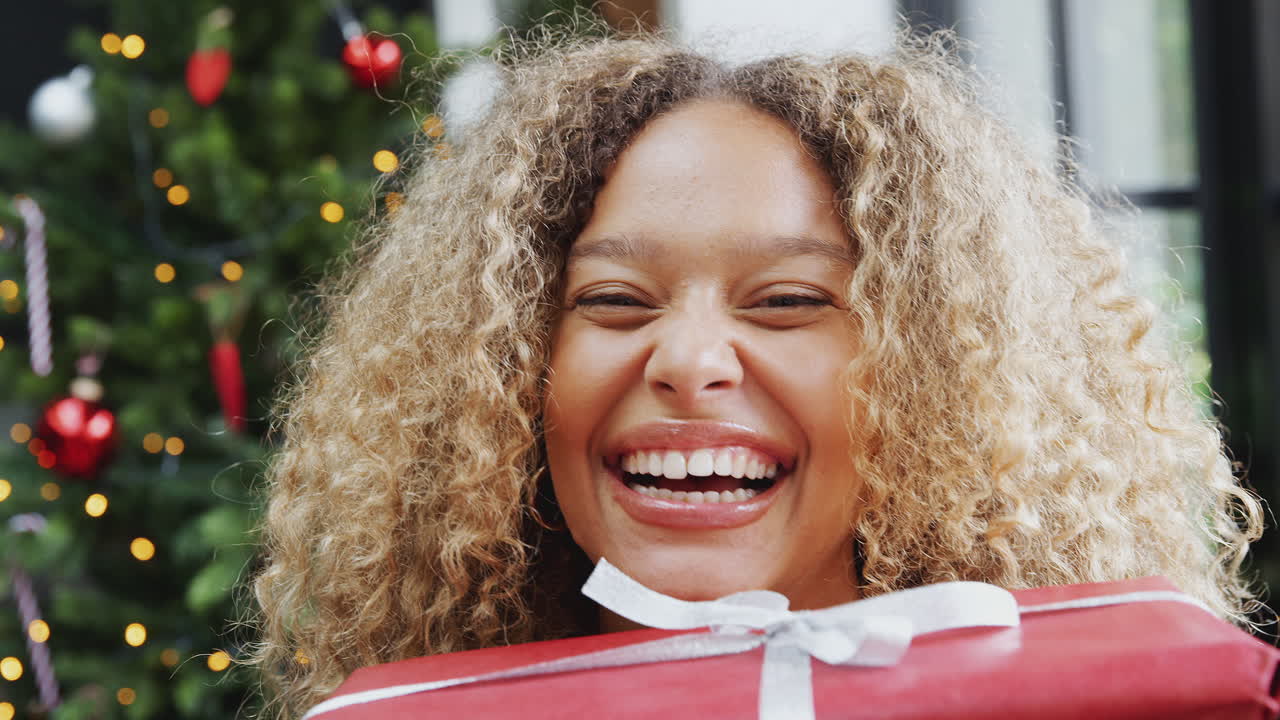retrato de una mujer que lleva una pila de regalos de navidad de pie junto al árbol en casa