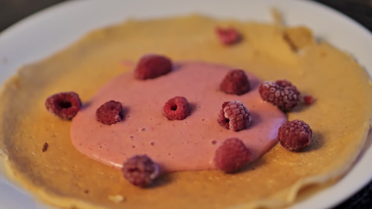 Pancake on a white plate with banana-strawberry sauce and frozen raspberries, 4K