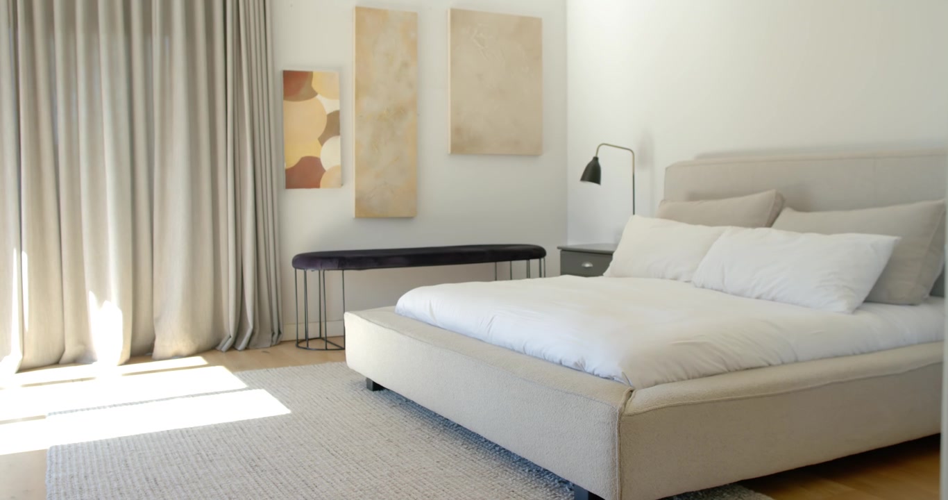 La telecamera si sposta a destra, rivelando il comodino mentre il letto rimane centrato e la luce del sole si restringe.